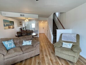 Ein Wohnzimmer mit einer Couch und einem Sessel, einem Essbereich und einer Treppe, die zu einer anderen Ebene führt.