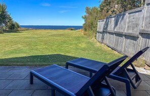 Eine Terrasse mit zwei Liegestühlen, die auf einen Rasen und einen Holzzaun blicken.
