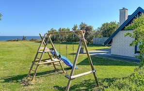 A wooden swing set in a grassy yard with a view of the ocean and a house with a chimney. - 3 bedroom cozy home in Fur (Fur)