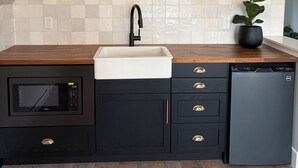 A kitchen with a microwave, sink, and dishwasher, wooden countertop, black cabinets, and a potted plant.