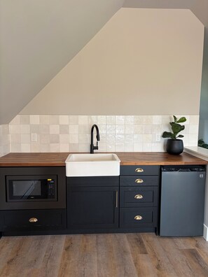 A kitchen with a microwave, sink, and dishwasher, wooden countertop, black cabinets, and a potted plant.