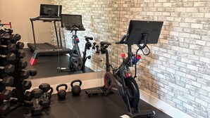 A gym with exercise equipment, a mirrored wall, and a brick-patterned wall.