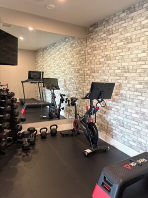 A gym with exercise equipment, a mirrored wall, and a brick-patterned wall.