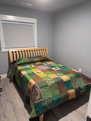 Ein Einzelbett mit hölzernem Kopfteil, eine Steppdecke mit Patchwork-Muster und ein Fenster darüber.