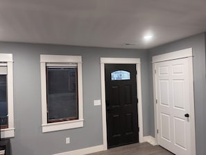 A hallway with a black door, a white door, and a window with a white frame.