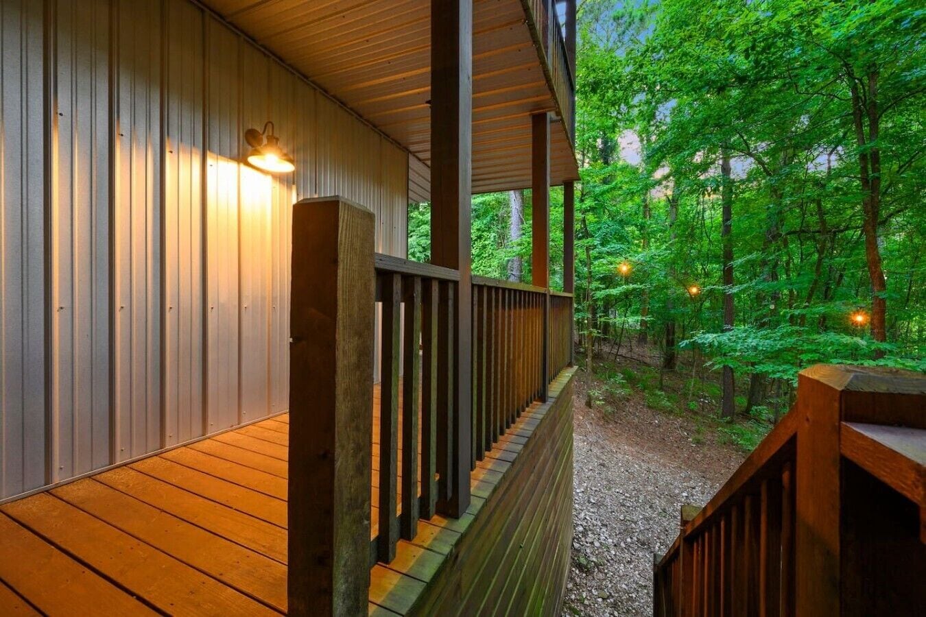 A wooden deck with a railing, surrounded by a forested area.