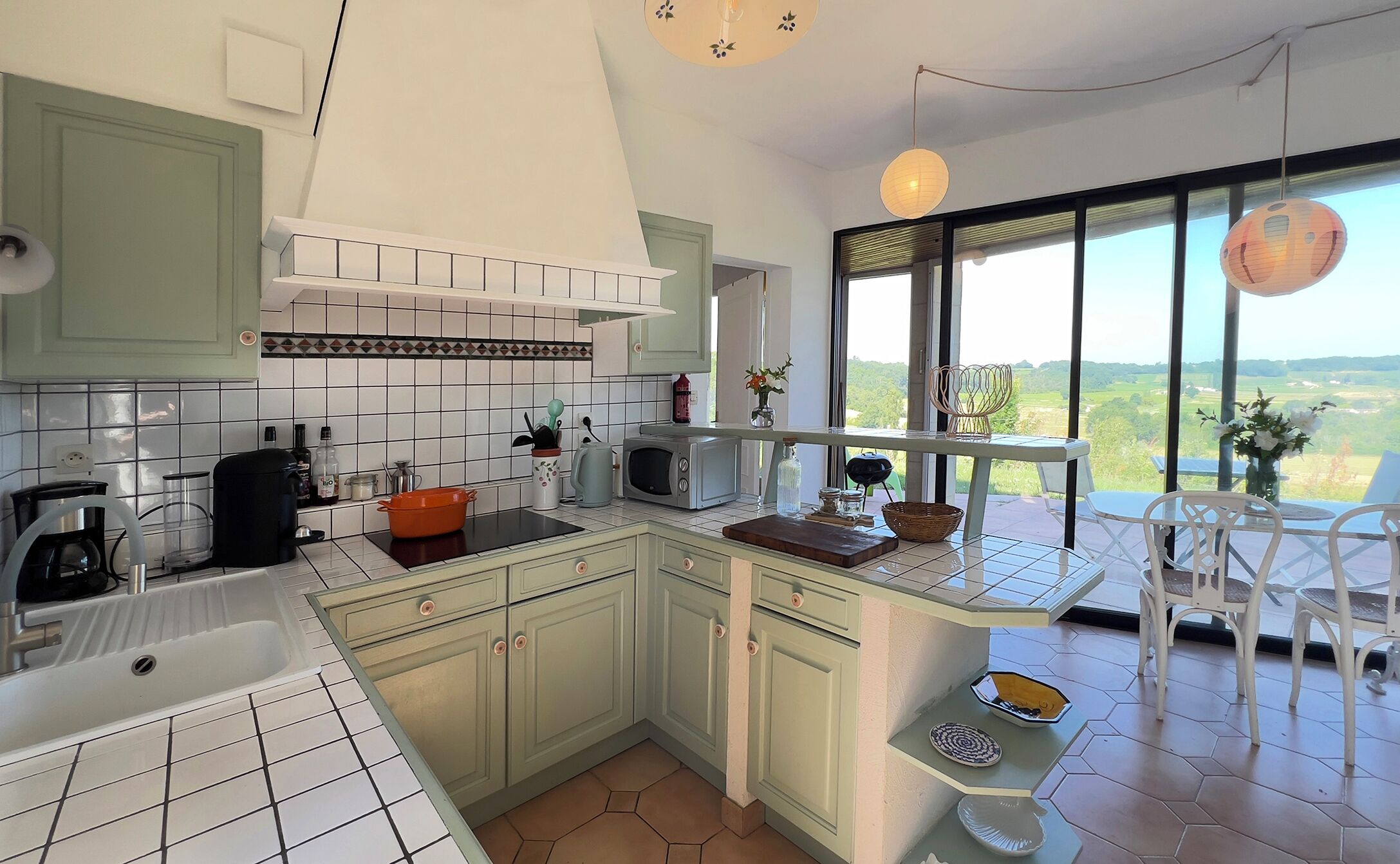A kitchen with a view of the countryside, a dining area with a table and chairs, and a small balcony with a chair.