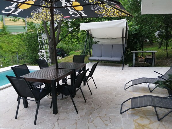 An outdoor patio with a pool, a table and chairs, a swing, and a covered seating area.