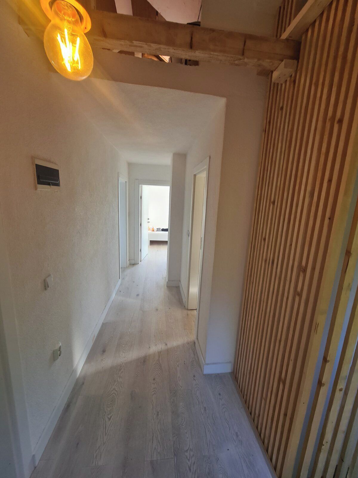 A hallway with wooden flooring, white walls, and a ceiling with exposed beams.