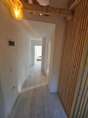 A hallway with wooden flooring, white walls, and a ceiling with exposed beams.