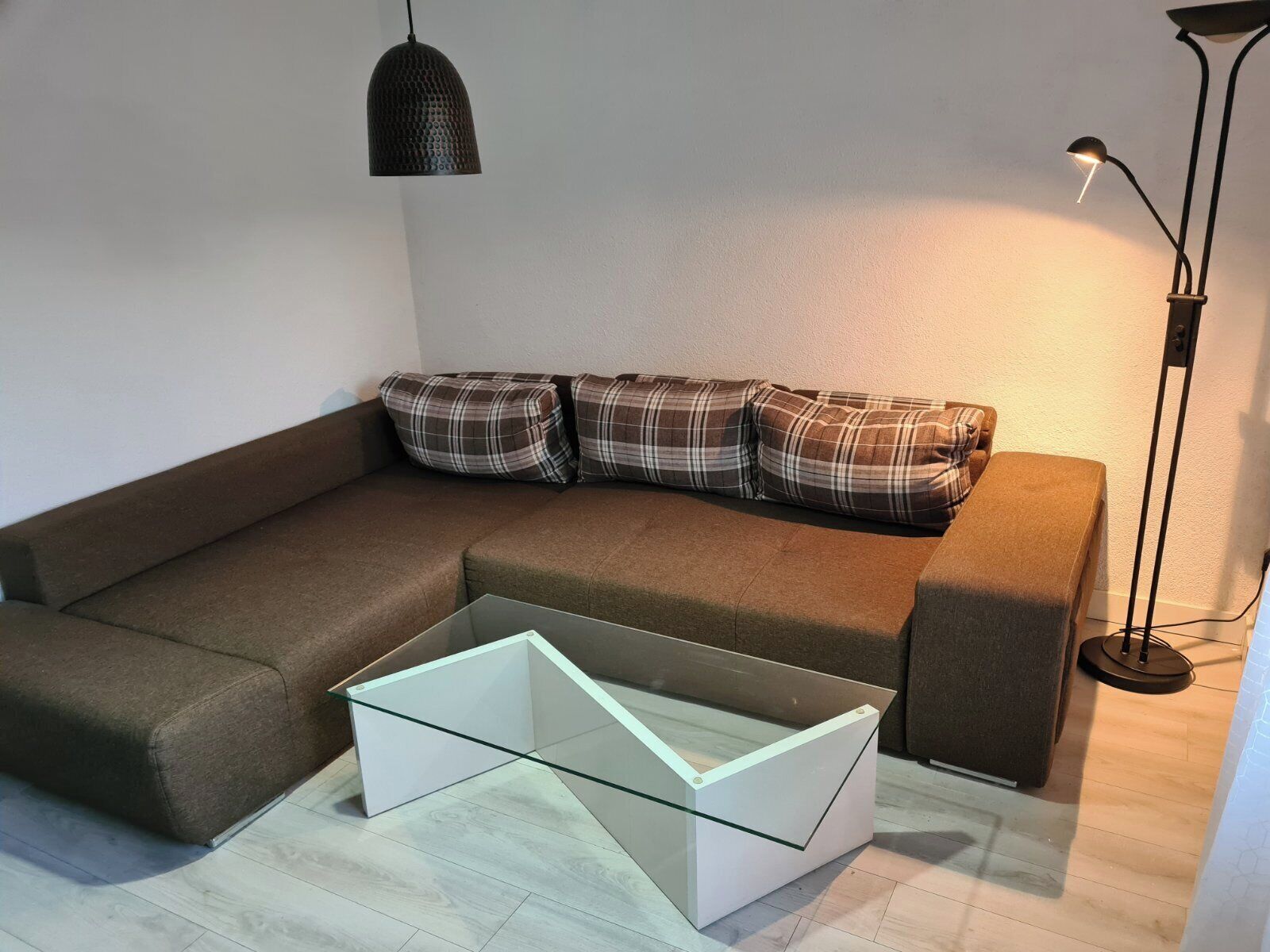 Uma sala de estar moderna com um sofá marrom, almofadas xadrez, uma mesa de centro de vidro e uma luminária pendente.