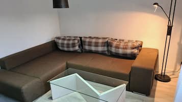 Uma sala de estar moderna com um sofá marrom, almofadas xadrez, uma mesa de centro de vidro e uma luminária pendente.