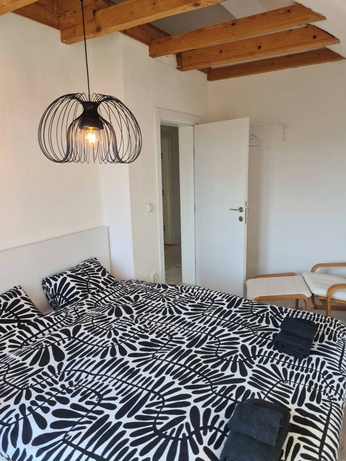 A bedroom with a bed, a chair, a door, and a hanging light fixture.