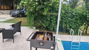 Um quintal com churrasqueira, móveis de pátio, piscina e um carro estacionado por perto.