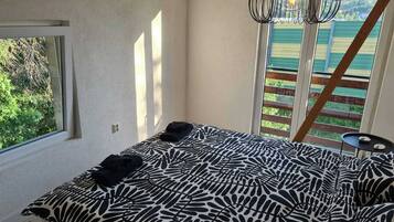 Quarto com cama, janela e vista para o verde.