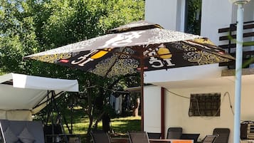 A swimming pool with lounge chairs and umbrellas, a tiled deck, and a building with a window.