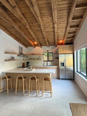 Eine moderne Küche mit Holzbalken, einer großen Kochinsel mit Barhocker und einem Edelstahlkühlschrank.