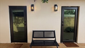 A black metal bench in front of a building with two black doors and two wall-mounted lights. - Private Miami home retreat with Oak Tree Deck & Gated Yard / 3 beds, 2 baths (Miami)