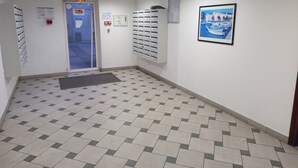 Un corridoio con pavimento piastrellato, una porta con stipite blu e una cassetta postale fissata al muro.
