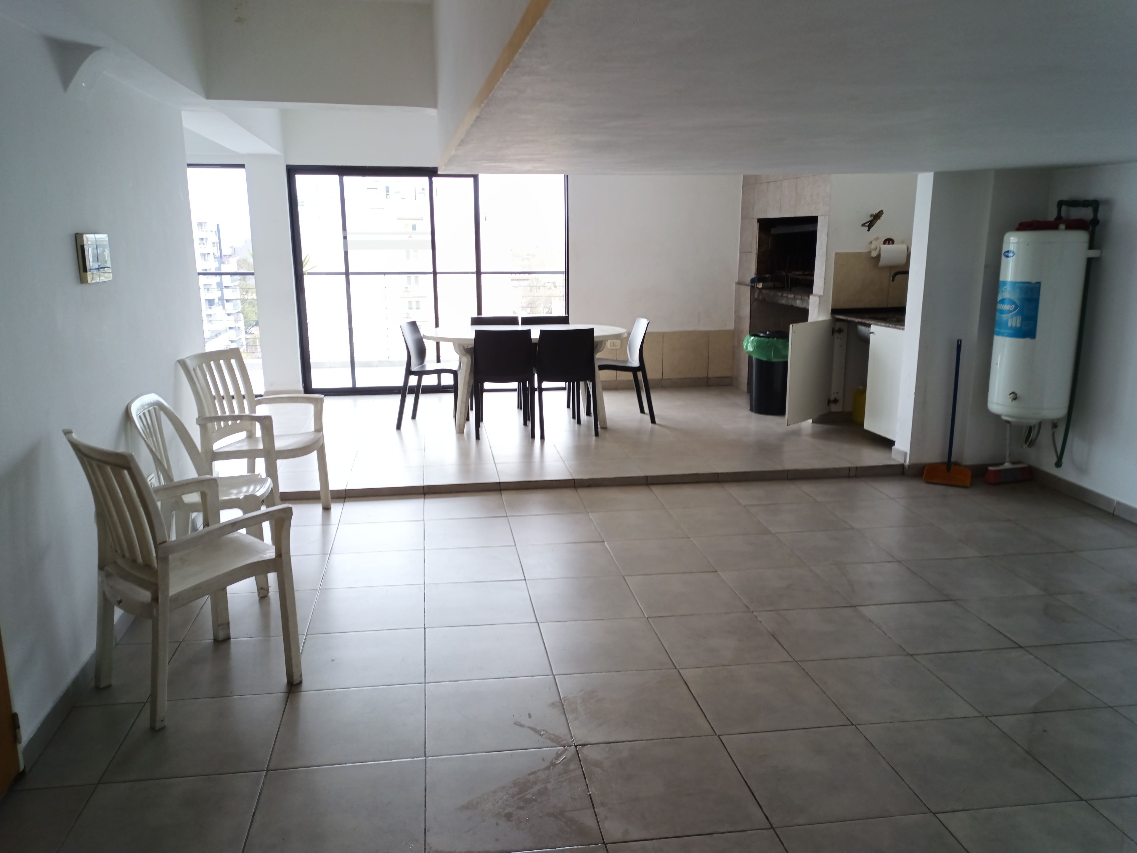 Una habitación amplia con zona de comedor, cocina y un gran ventanal que proporciona luz natural.