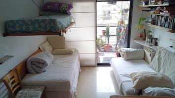 A compact room with two beds, a small table, and a shelf with books and plants.