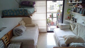 A compact room with two beds, a small table, and a shelf with books and plants. - One apartment - A lot of beds at Palermo Hollywood - Fully equiped - ב''ה (Buenos Aires)