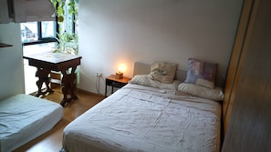 A bedroom with a bed, a bedside table with a lamp, a wooden desk, and a window with plants. - One apartment - A lot of beds at Palermo Hollywood - Fully equiped - ב''ה (Buenos Aires)