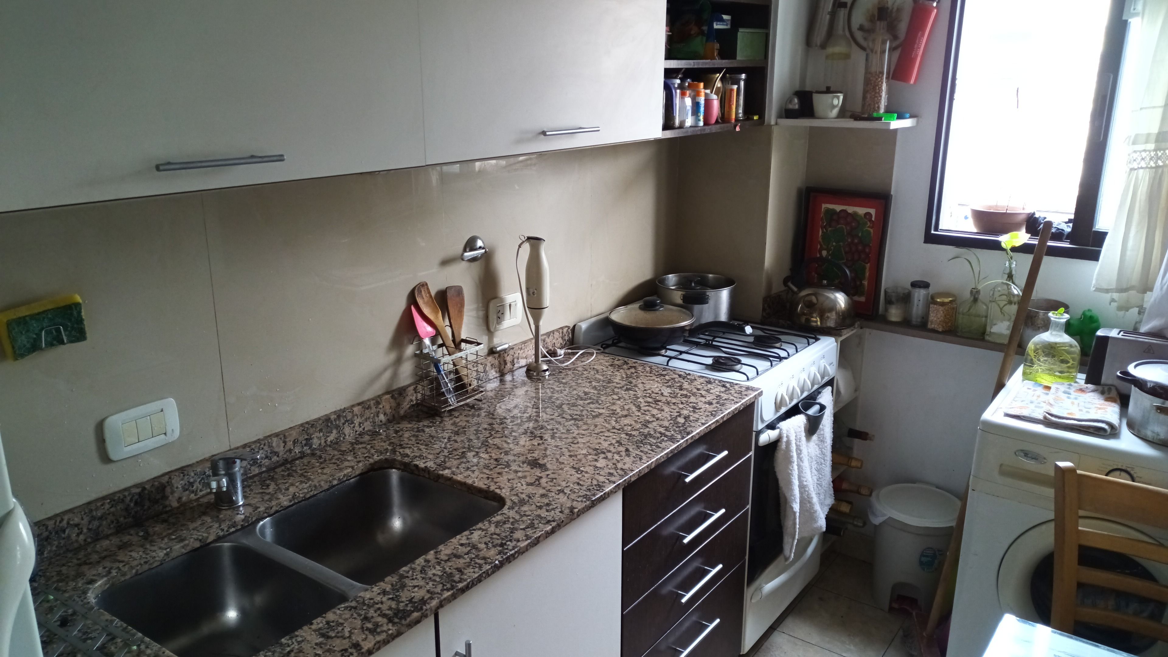 Una cocina con encimeras de granito, un lavabo doble, una estufa y una ventana pequeña.