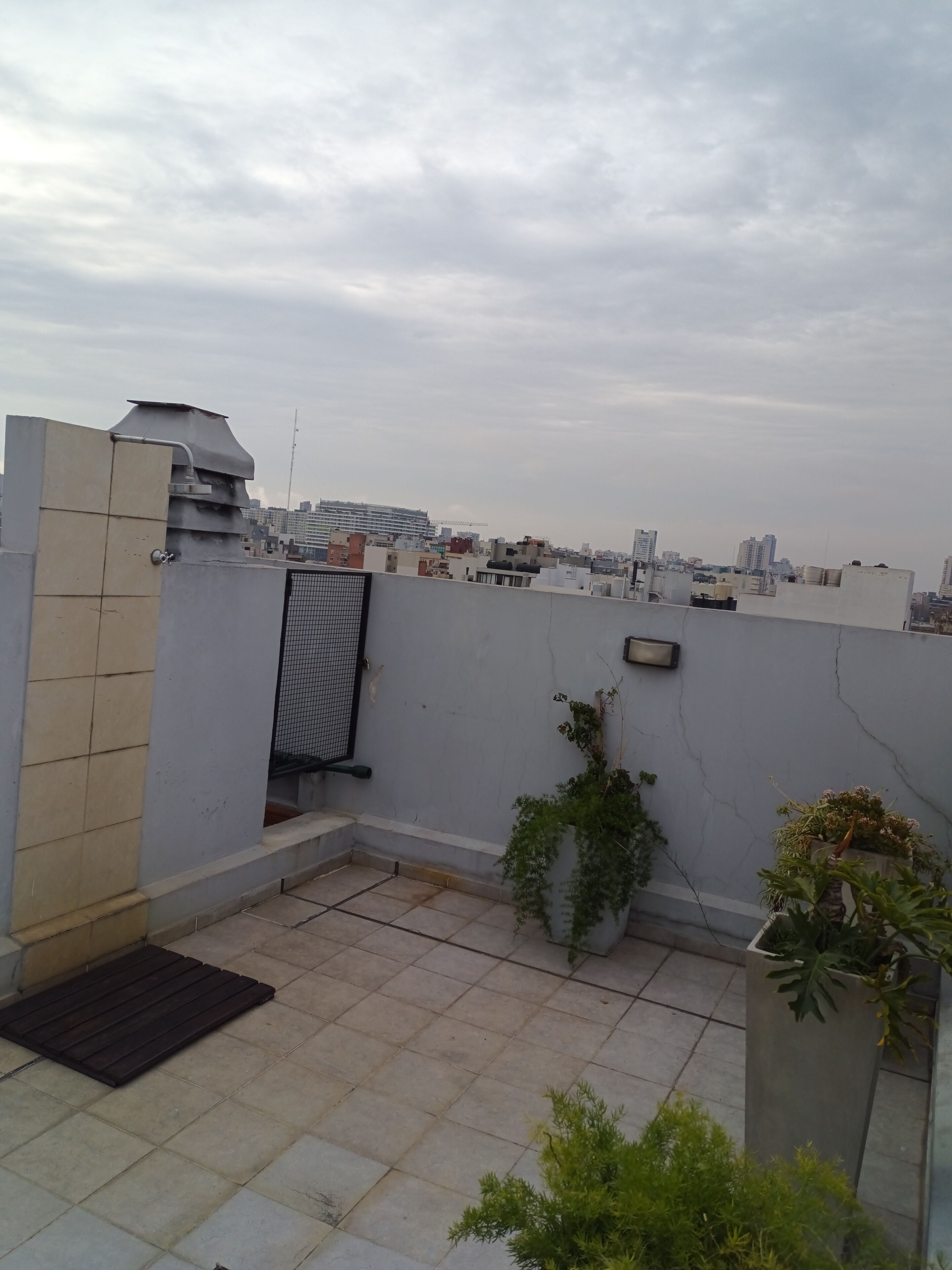 A rooftop terrace with a view of a cityscape, a metal gate, and potted plants.