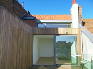 Un edificio moderno con facciata in legno, una porta in vetro che dà su un ambiente interno e un tetto con tegole rosse.