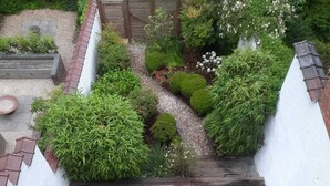 A wooden deck leading to a white wall with a garden area featuring various plants and a gravel path. - Abbaye de la Cambre • Private Mansion • 469 m• Lift &  AIR CO , Min 92 nights (Ixelles)