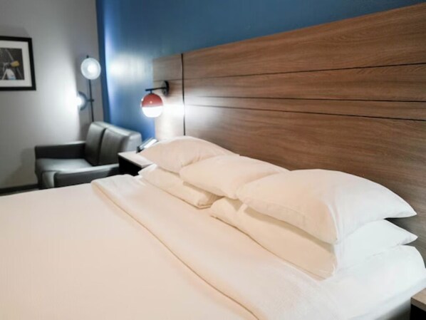Ein Hotelzimmer mit Holz-Kopfteil, einem Bett mit weißen Leinentüchern, einem Nachttisch mit Lampe und einem gerahmten Bild an der Wand.
