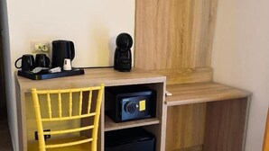 A compact room with a desk, a chair, a coffee maker, a radio, and a small black storage unit. - Mia Napoli (Naples)