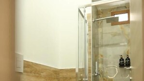 A bathroom with a glass-enclosed shower, a toilet, and a marble-tiled wall. - Mia Napoli (Naples)