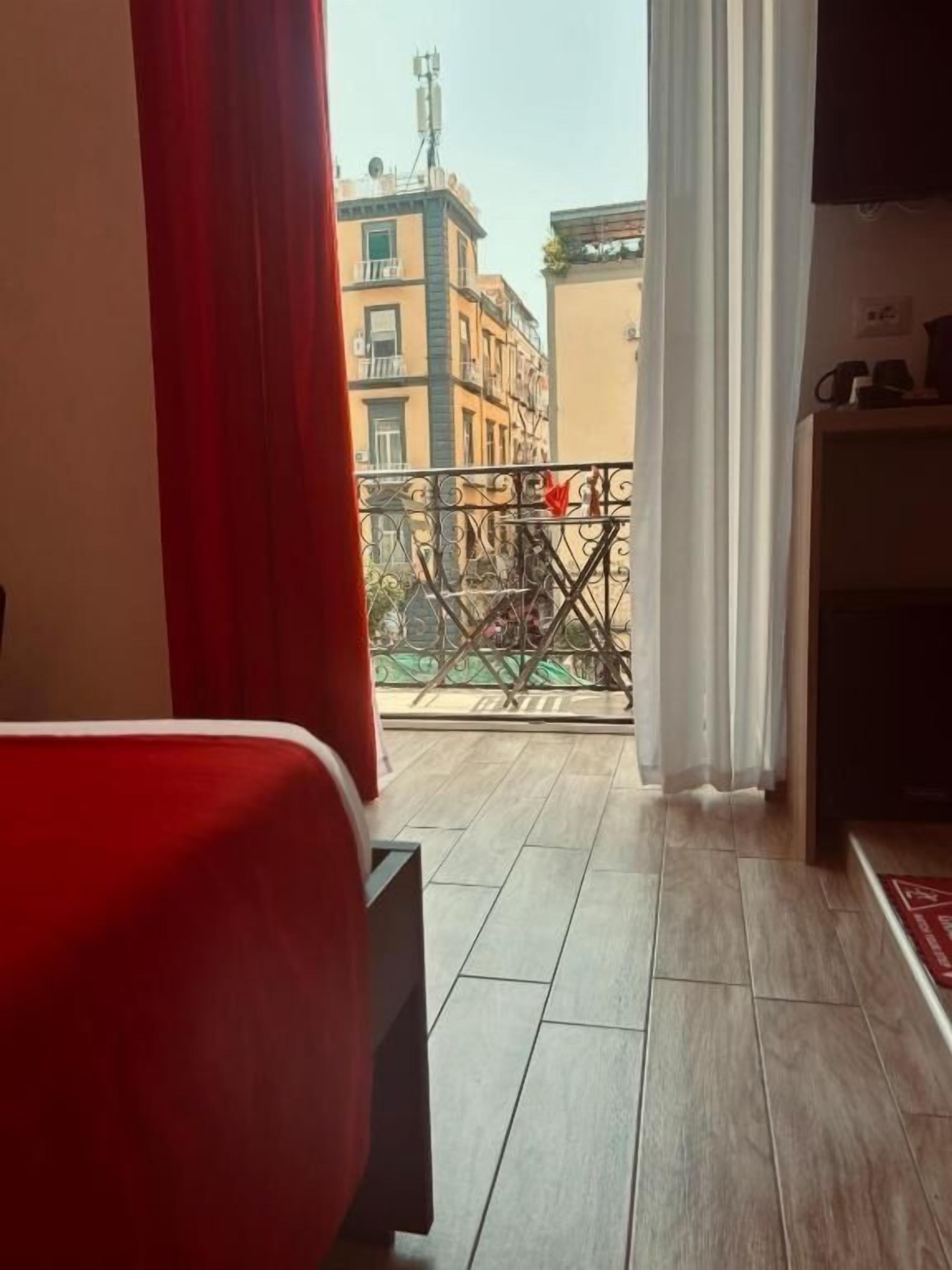A hotel room with a balcony, a red chair, and a television on a stand.