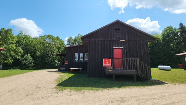 En enkel, rustik träbyggnad med en röd dörr, en skylt som förbjuder parkering och ett picknickbord.