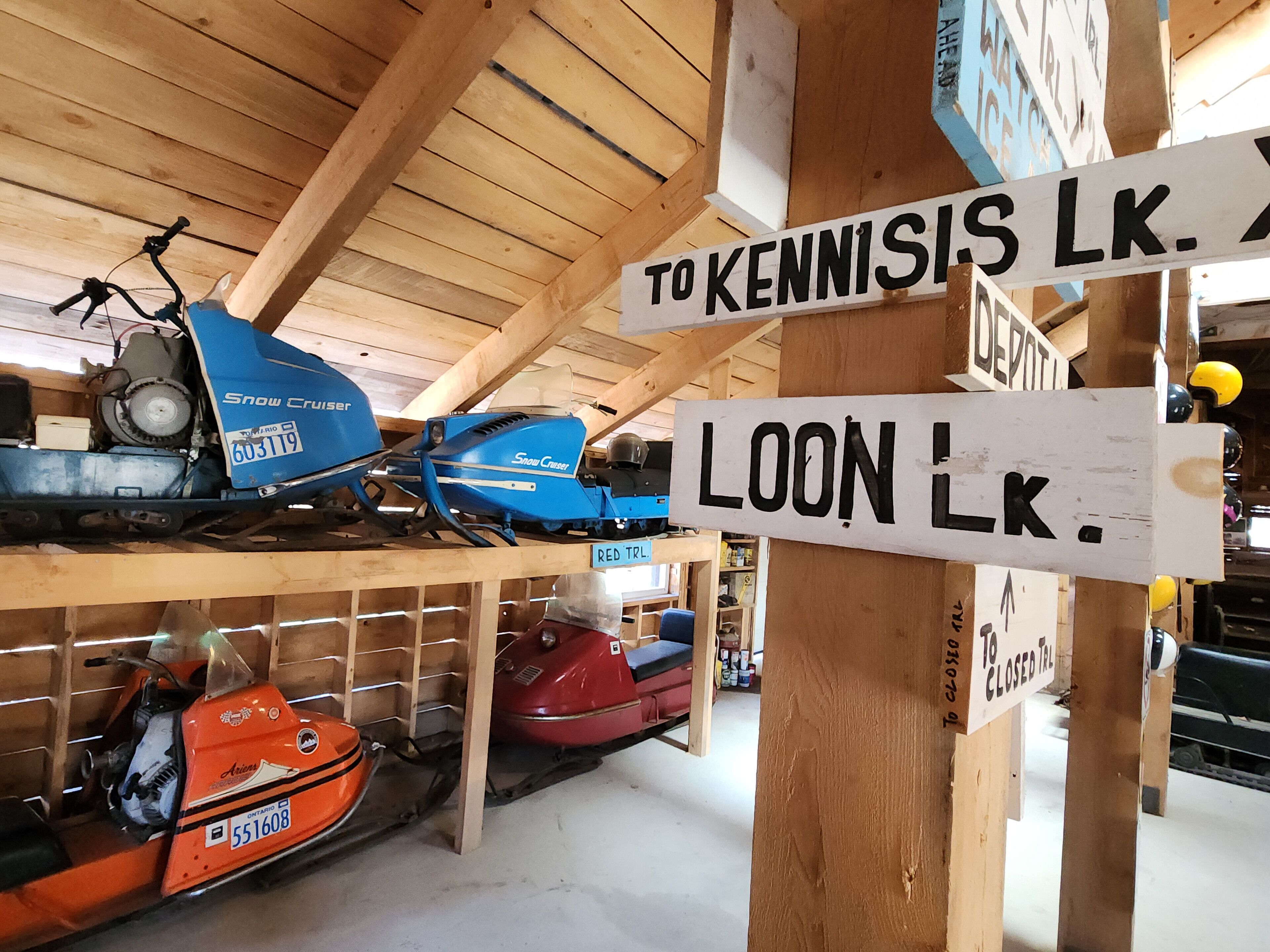 Une collection de motoneiges et un panneau indicateur indiquant les directions vers le lac Kennisis et le dépôt.