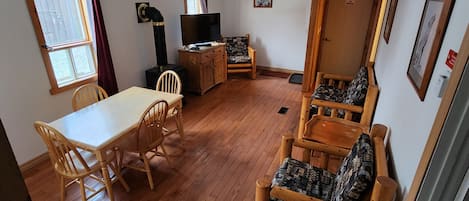 Habitación acogedora con una mesa de madera, sillas, sofá, chimenea y una puerta con un letrero.