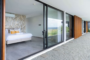A modern bedroom with a large bed, a view of the sea through floor-to-ceiling glass doors, and a patterned wall. - Villa Coral Breeze | Luxury Villa | Private Beach (Willemstad)