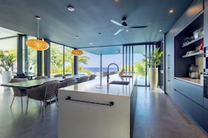 Una cocina moderna con una isla grande, electrodomésticos integrados y vista al océano.