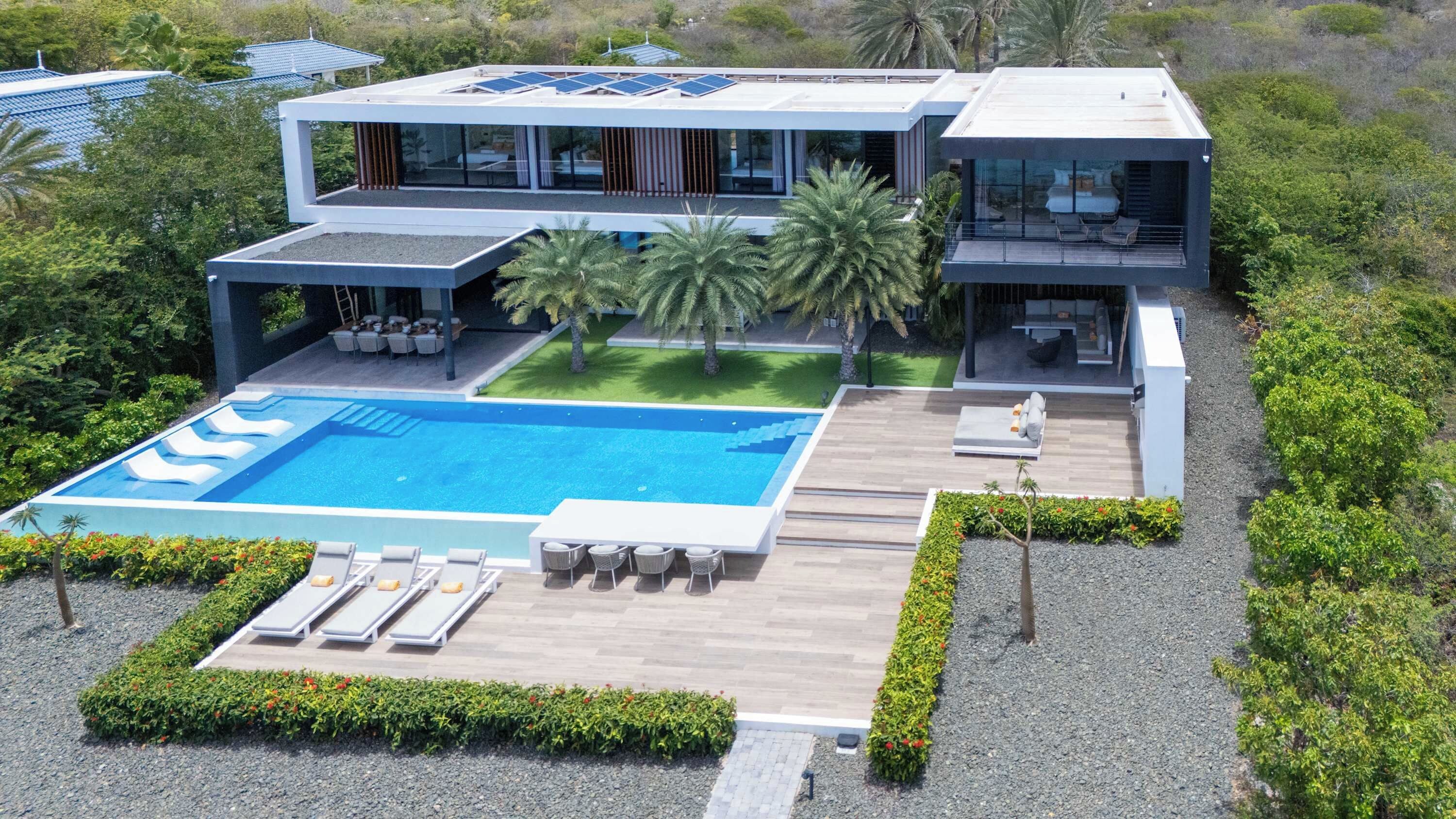 Ein modernes Haus mit Swimmingpool, Sitzgelegenheiten im Freien und Solaranlage.