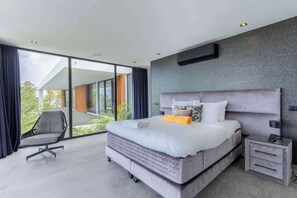 A modern bedroom with a large bed, a chair, a nightstand, and a view of the outdoors. - Villa Coral Breeze | Luxury Villa | Private Beach (Willemstad)
