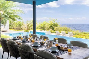 A dining table set for breakfast with a pool and ocean view. - Villa Coral Breeze | Luxury Villa | Private Beach (Willemstad)