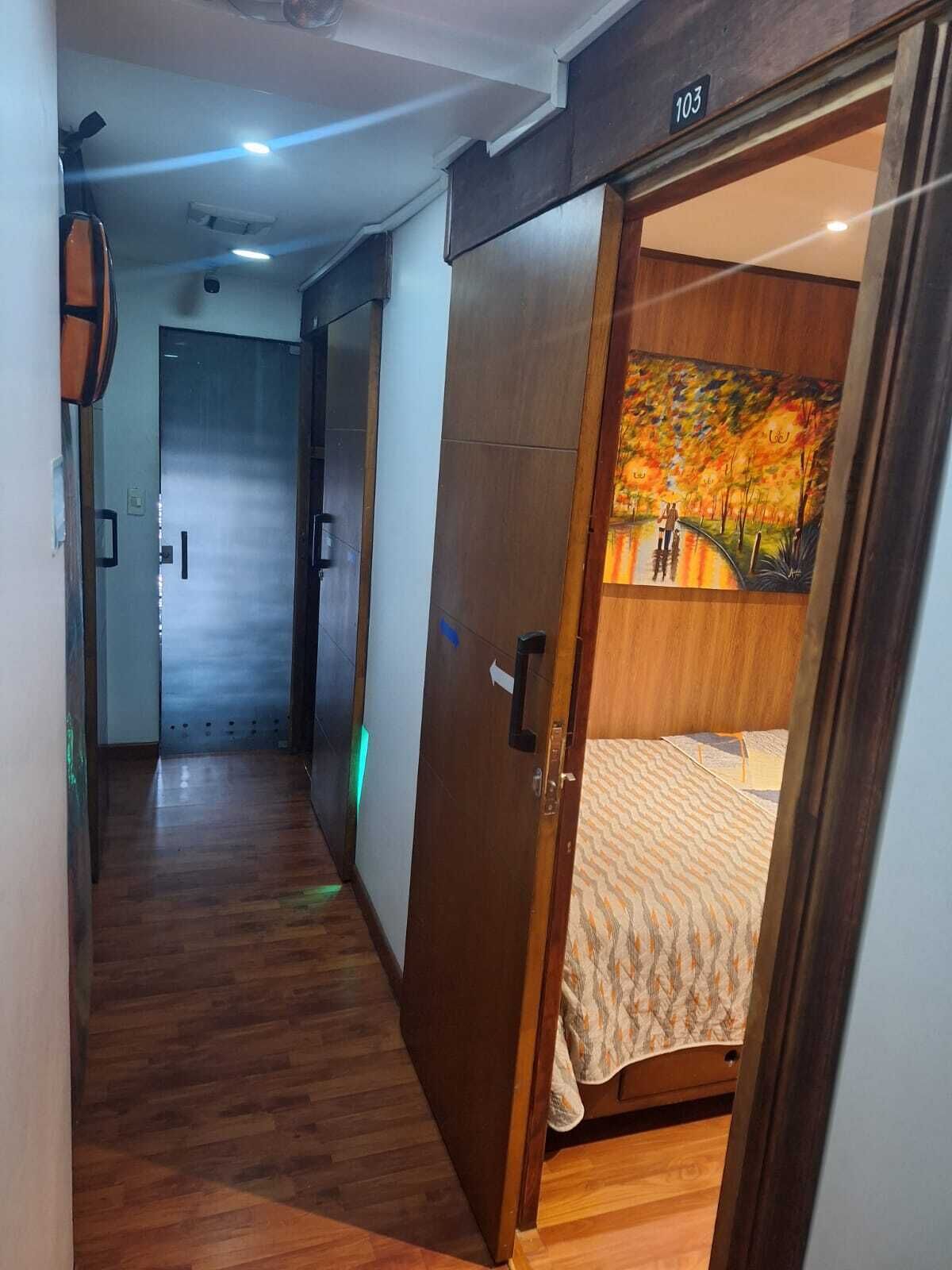 A hotel room with a wooden door, a bed with a patterned bedspread, and a painting of a landscape on the wall.