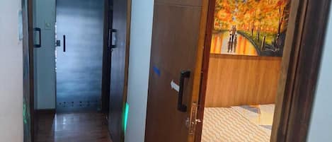 Una habitación de hotel con puerta de madera, una cama con colcha estampada y un cuadro de un paisaje en la pared.