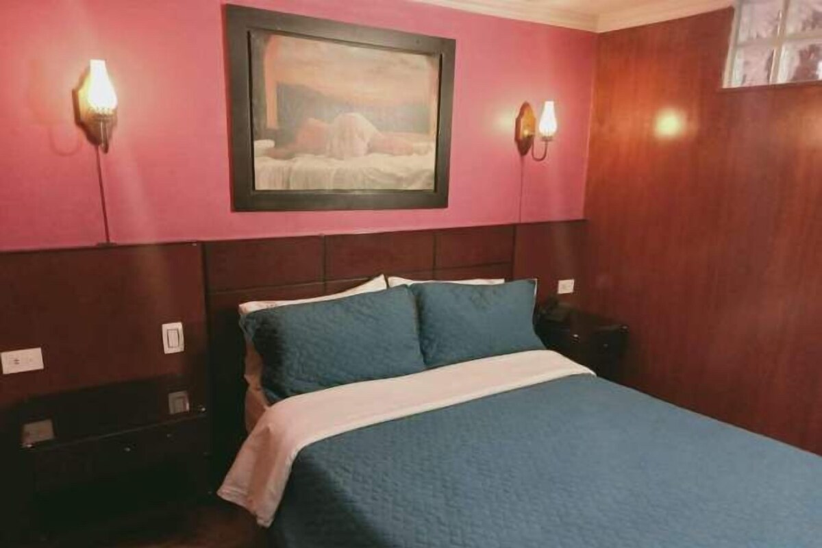 A hotel room with a bed, a nightstand, and wall-mounted lamps.