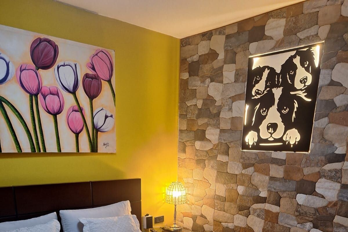 Ein Hotelzimmer mit Bett, Nachttisch, Lampe, einem Blumenbild und einer Steinwand.