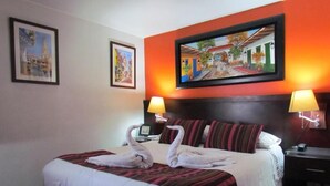 A hotel room with a bed, two wall-mounted lamps, and a painting above the bed. - Hotel Apartasuite Normandia (Bogotá)