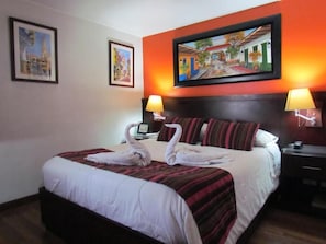 Habitación de hotel con una cama, dos lámparas fijadas a la pared y un cuadro sobre la cama.