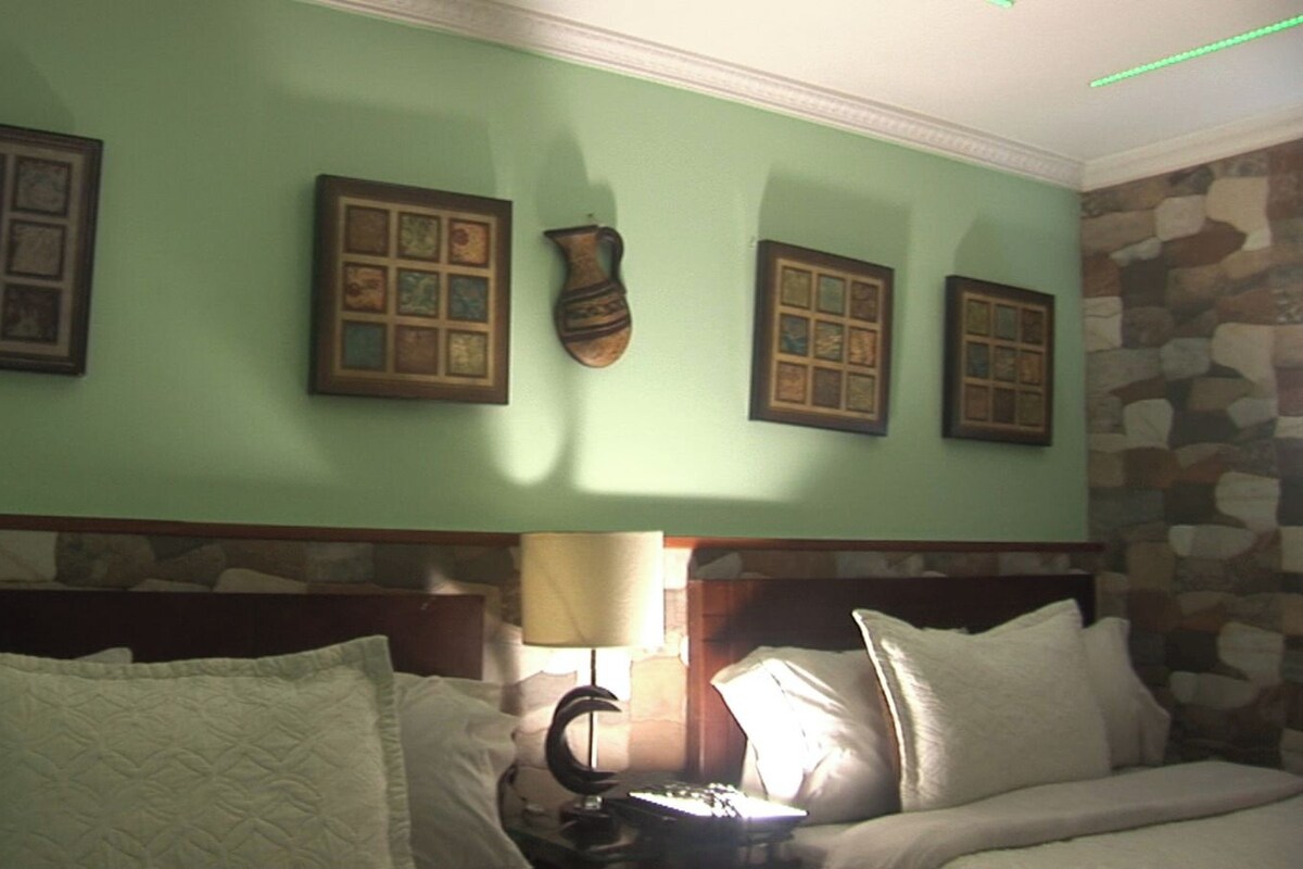 A hotel room with a bed, pillows, a lamp, and framed pictures on the wall.